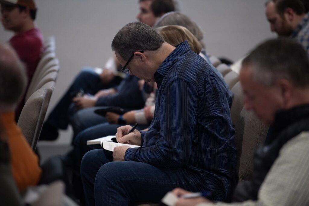 A man, seated, writes in a notebook resting on his lap at Risen Hope Church in Summerville, SC